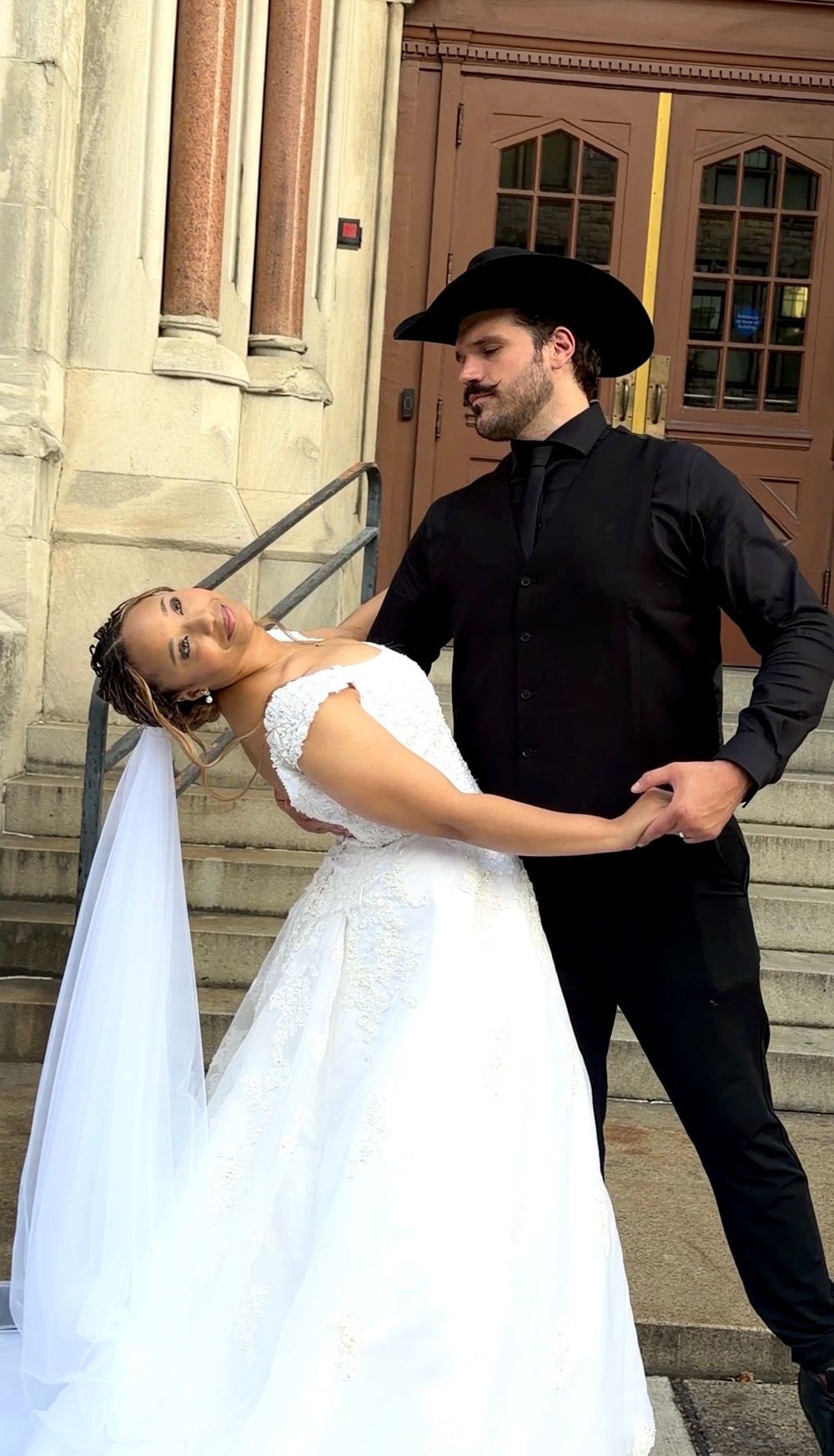 Austin Jauregui dipping a bride in a white gown and veil on stone church steps
